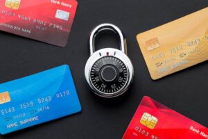 A silver combination lock sits center, surrounded by various credit cards on a black background, symbolizing financial security.