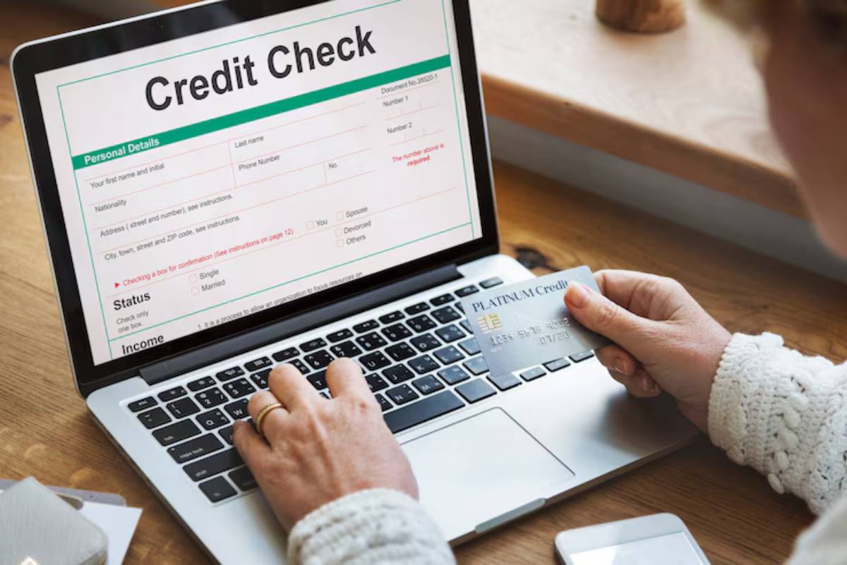 A person holding a credit card while filling out an online credit check form on a laptop, with a wooden table in the background. 