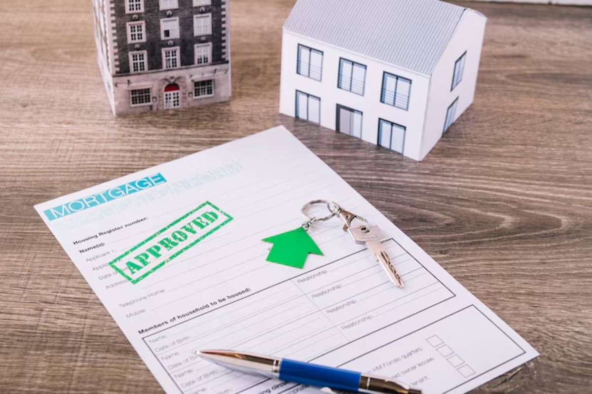 A mortgage approval document with a green Approved stamp, keys, and miniature houses on a wooden surface. 