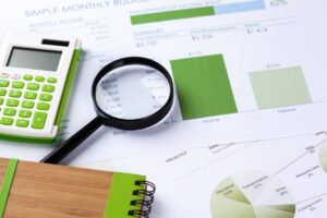 A calculator, magnifying glass, and financial documents displaying a monthly budget summary, income, and expense breakdown graphs.