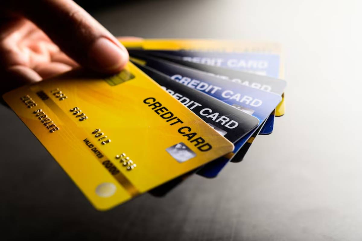 A hand holds multiple credit cards, featuring yellow and black designs, against a softly lit background.