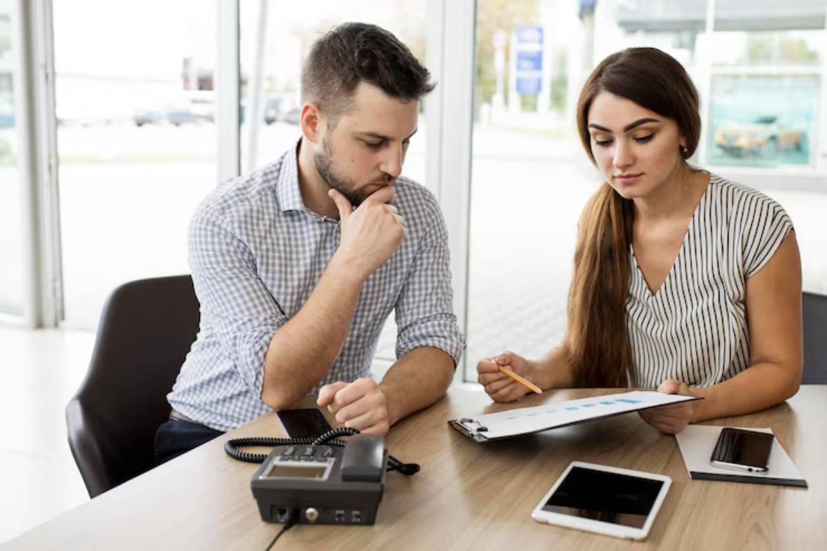  Two professionals discuss charts and data during a meeting, with a telephone and tablets visible on their work table.