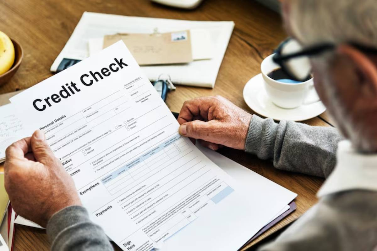  An elderly man reviews a credit check form while seated at a wooden table with a coffee cup and a bowl of bananas nearby.