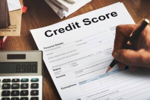 A hand writing on a Credit Score form with a calculator displaying 8980 in the foreground, surrounded by papers and a wallet.