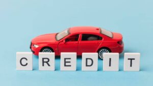 A red toy car beside white blocks spelling CREDIT against a light blue background, symbolizing financing or auto credit.