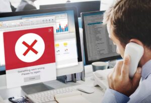 A frustrated man on the phone faces a computer error message reading, Something went wrong. Please try again. on his desk.