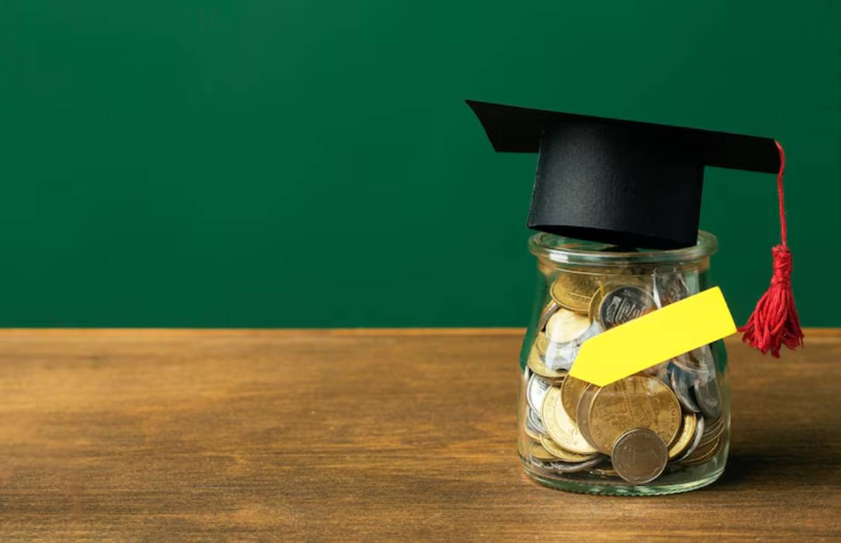 A glass jar filled with coins, topped with a graduation cap, symbolizing savings for education against a green background. 