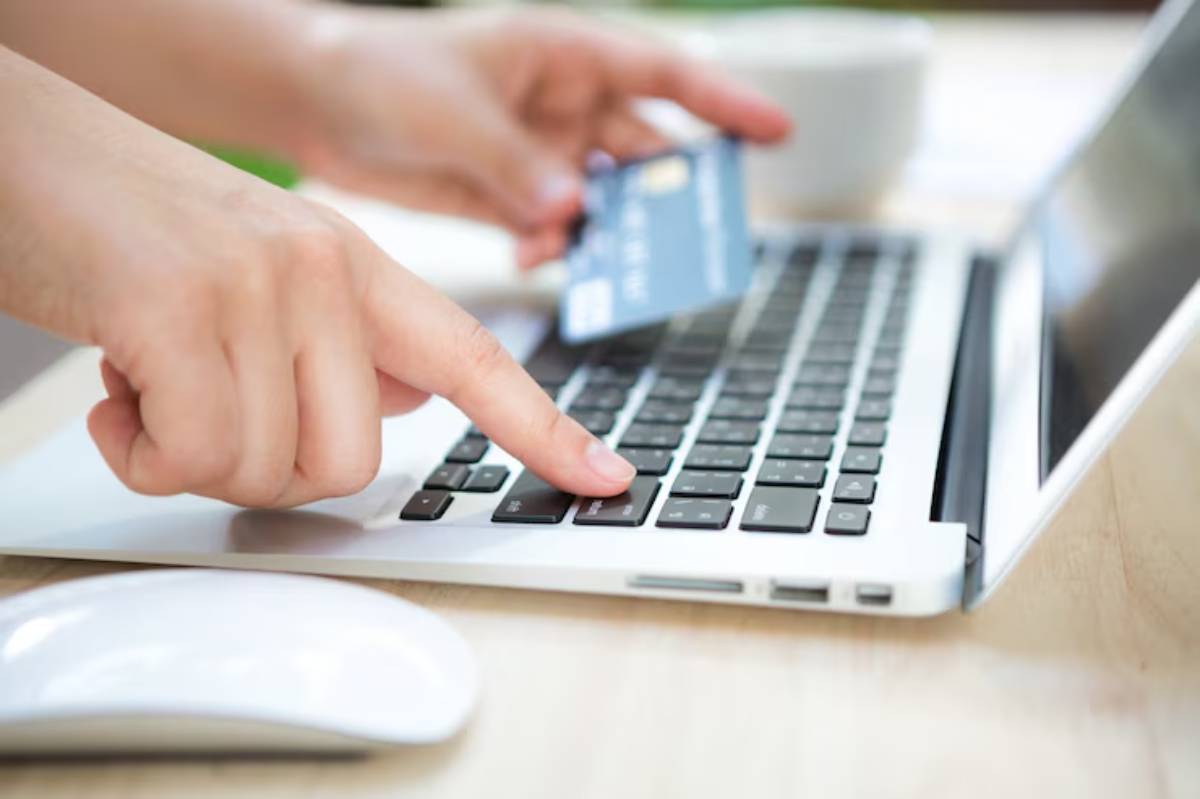  A person uses a credit card to make an online purchase, typing on a laptop's keyboard with a computer mouse nearby.