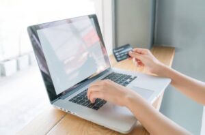 A person using a laptop, entering information while holding a credit card, with a bright, airy background.