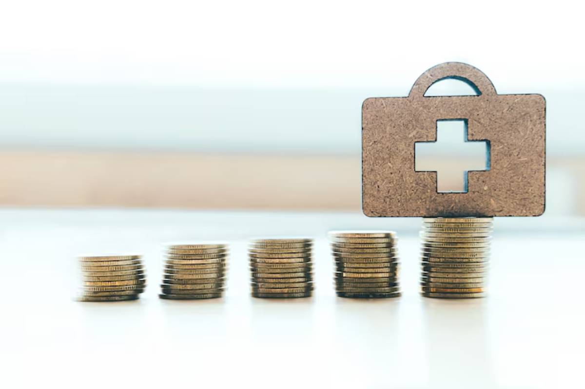 Stacks of coins with a wooden medical cross box on top, symbolizing health investment and financial growth in healthcare.