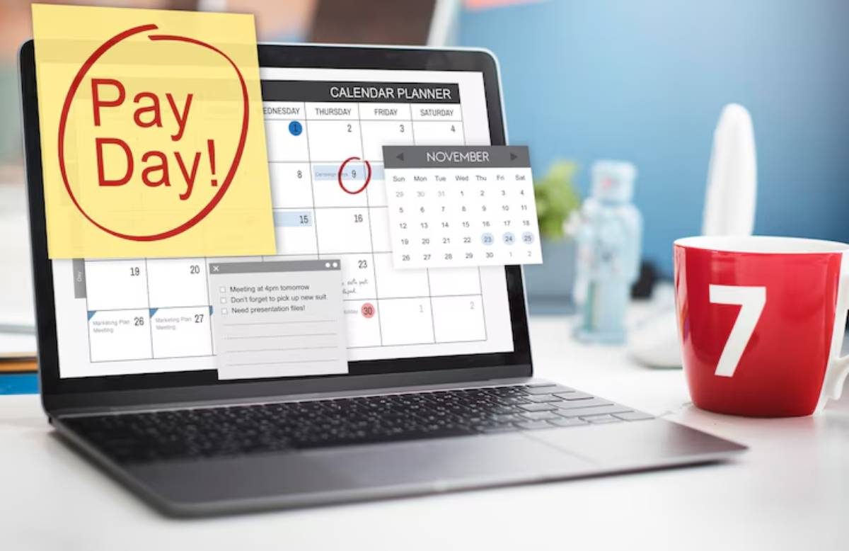 A laptop shows a calendar marked Pay Day with sticky notes and reminders, beside a red mug with the number 7. 