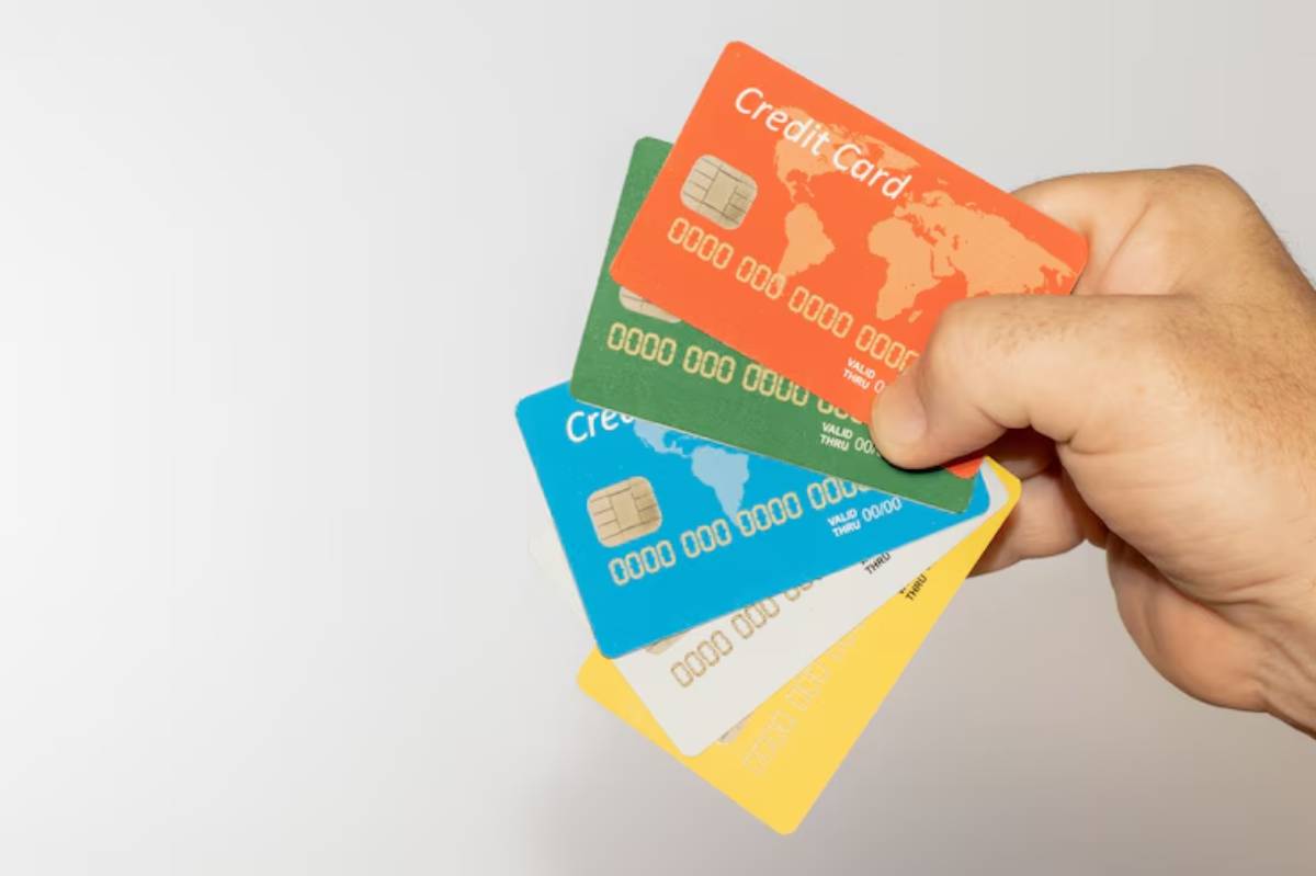 A hand holds four colorful credit cards against a light background, showcasing a variety of designs and colors.