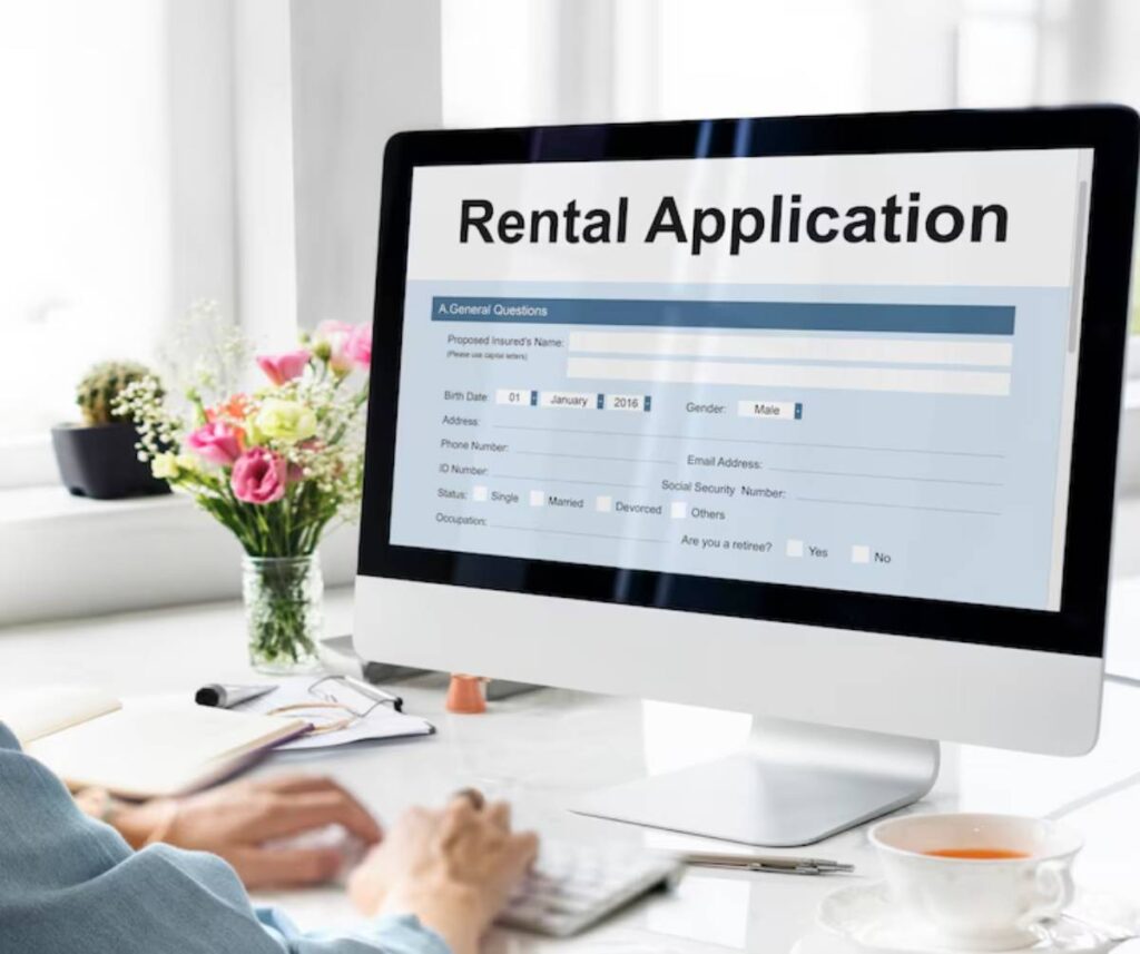 A person fills out a rental application on a computer, with a floral arrangement and a cup of tea on a desk nearby.