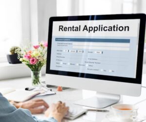 A person fills out a rental application on a computer, with a floral arrangement and a cup of tea on a desk nearby.