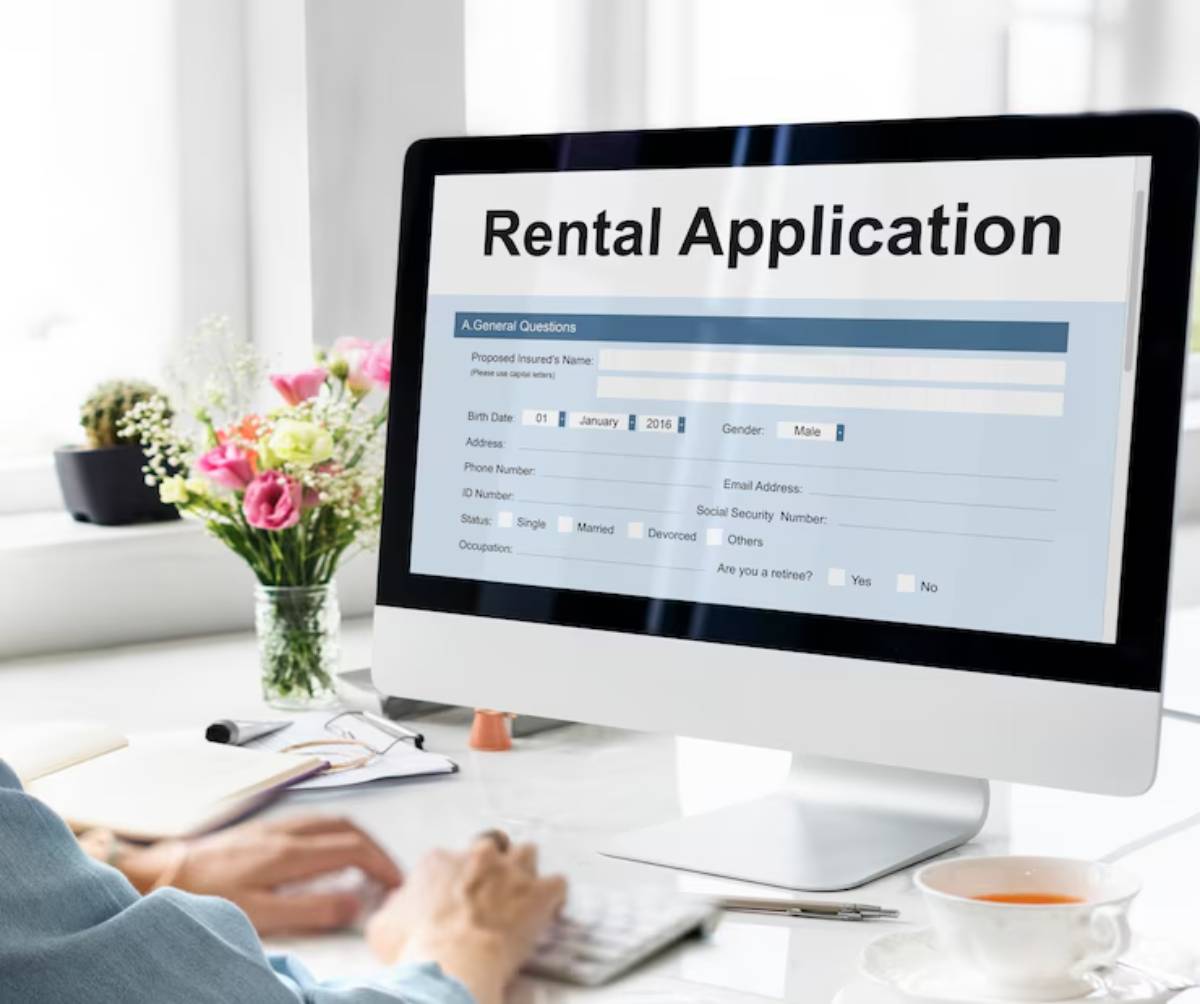 A person fills out a rental application on a computer, with a floral arrangement and a cup of tea on a desk nearby.