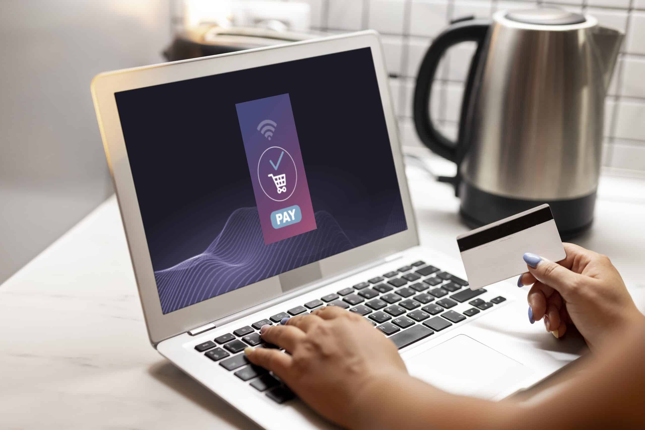 A person holds a credit card while making an online payment on a laptop, with a payment interface displayed on the screen.