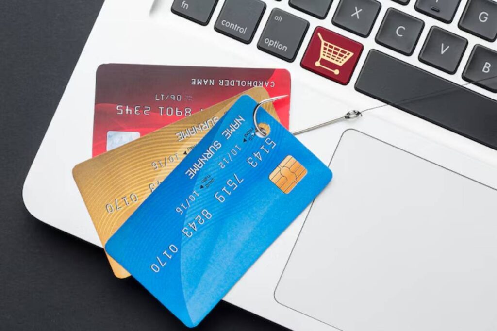 Three credit cards in blue, gold, and red next to a laptop keyboard, illustrating online shopping and payment methods.