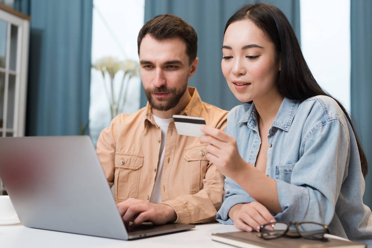  A man and woman are seated at a table, using a laptop, with the woman holding a credit card, focused on their online activity.